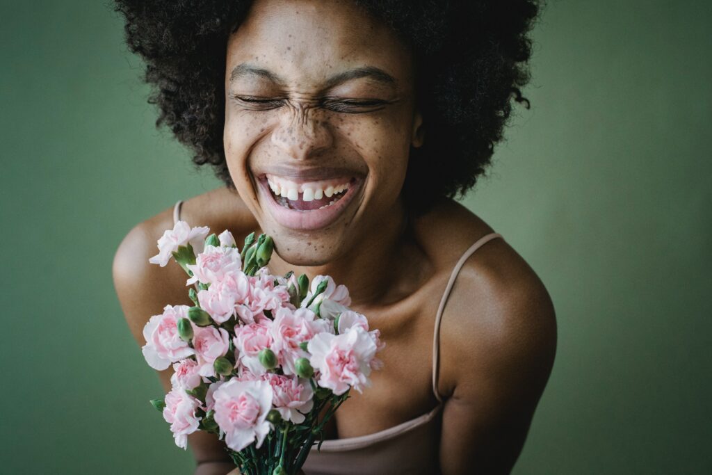 Image sur fond vert foncé d'une femme noire qui sourit et qui tient un bouquet de fleurs roses