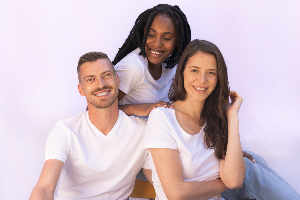 1 jeune femme noir soir aux côtés d'une femme et d'un monsieur. Ils portent tous un tee-shirt blanc et ils sourient.