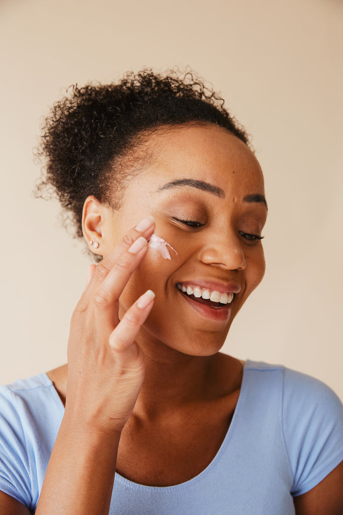 femme métisse avec un haut bleu ciel qui se mets de la crème sur la joue droite